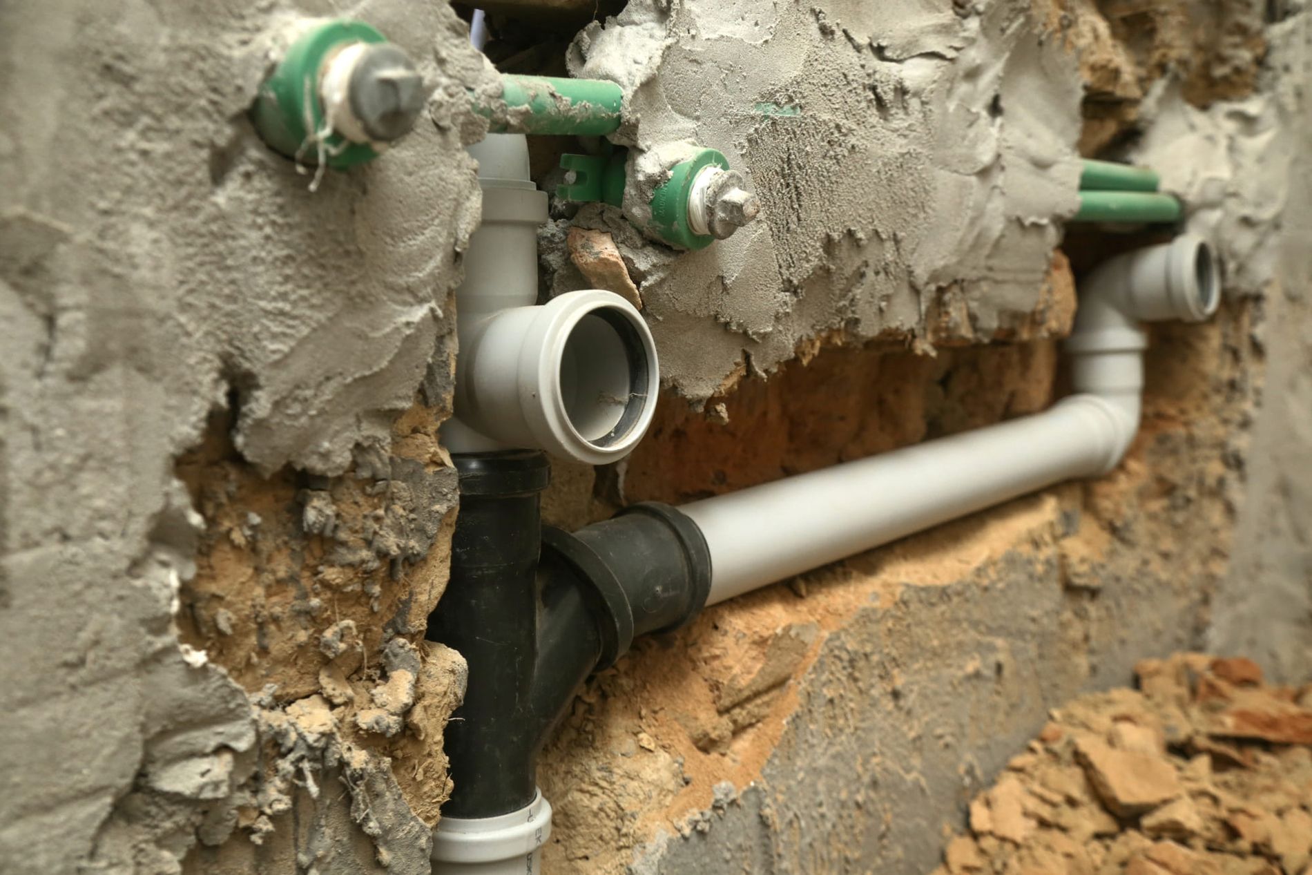 Freigelegte Abwasserrohre und Wasserleitungen in einer aufgestemmten Wand während einer Rohrsanierung