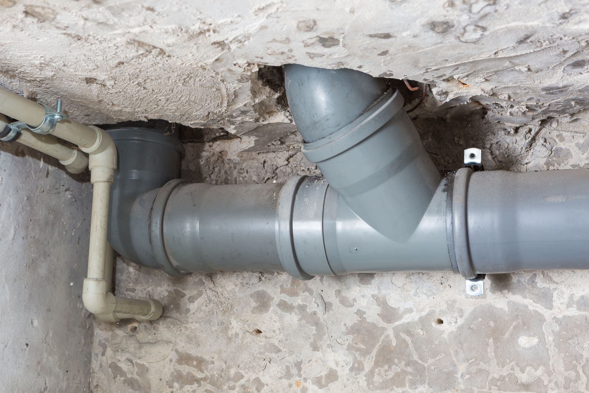 Graue Abwasserrohre mit Bogen und Abzweig unter einer Kellerdecke montiert